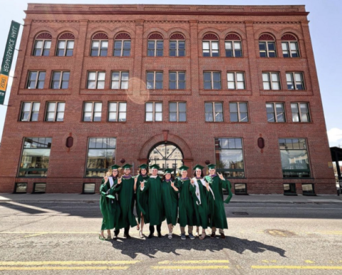 Students in cap and gown in front of downtown NDSU building